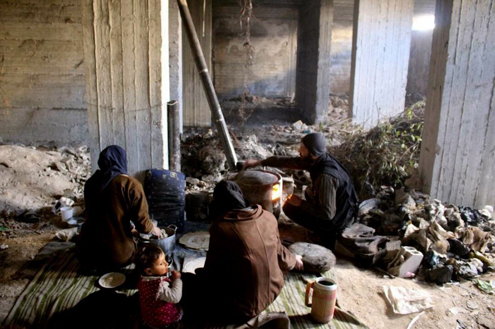A family prepares to make a meal in a destroyed house, used as an emergency shelter, after being displaced from their home in Eastern Ghouta.